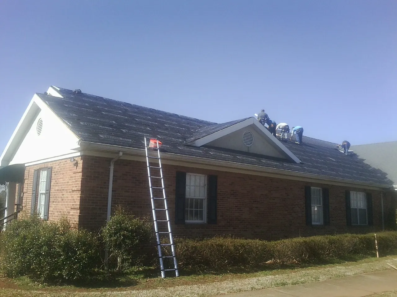 Crew tearing shingles off a brick ranch roof with a ladder set — Metal Roof Repair work by our crew in Moxahala
