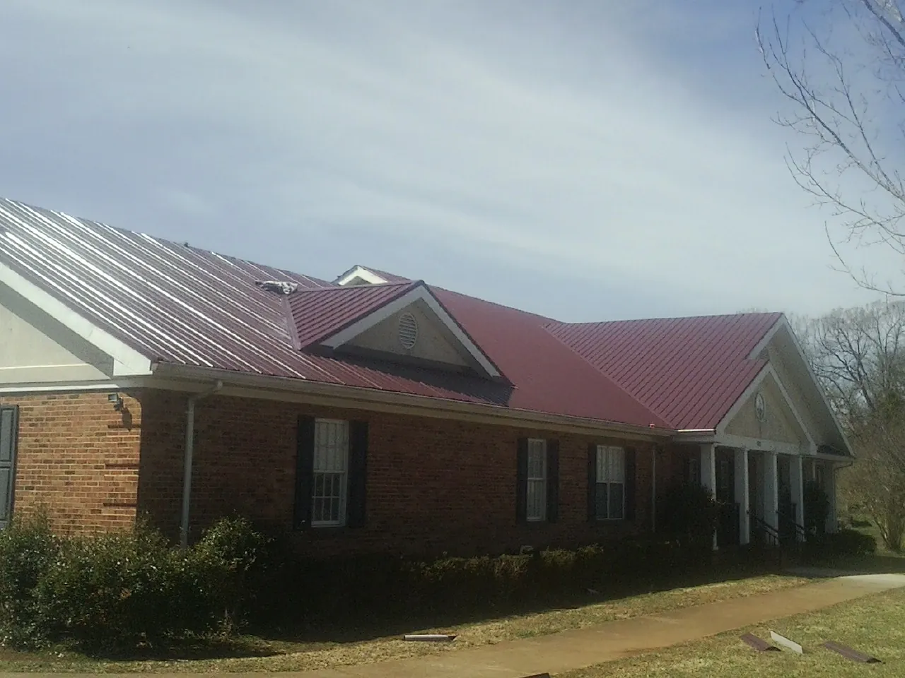 Red metal roof with gabled entries on a long brick building, from a Hail Damage Roof Repair job in Moxahala