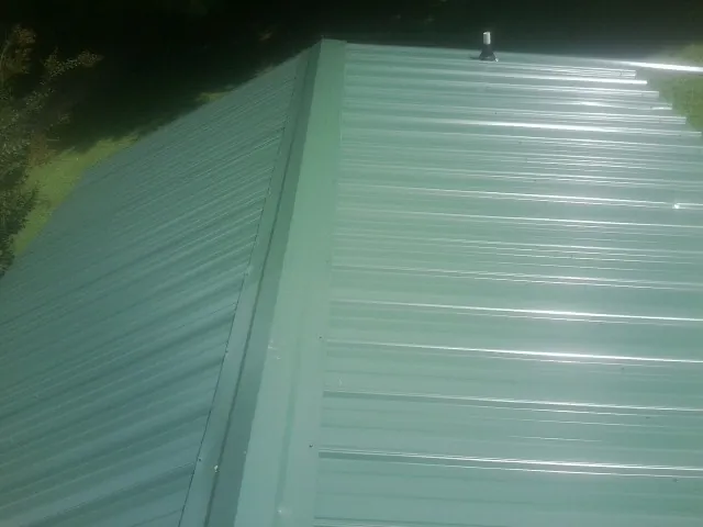 New green metal panels meeting at the ridge of a roof — Flat Roof Repair work by our crew in Moxahala