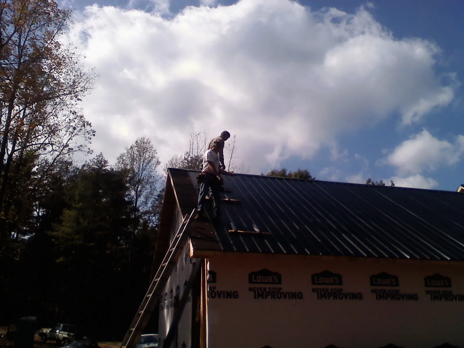 Roofer fastening dark metal panels high against a cloudy sky, from a Roof Inspection job in Moxahala