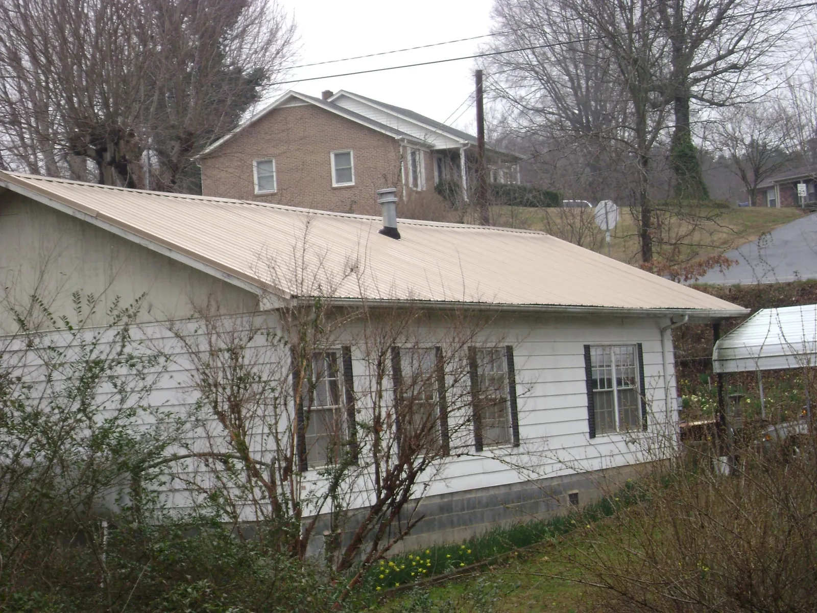 Tan metal roof on a white sided house set into a hillside — Commercial Roofing by Roofing Brothers in Moxahala